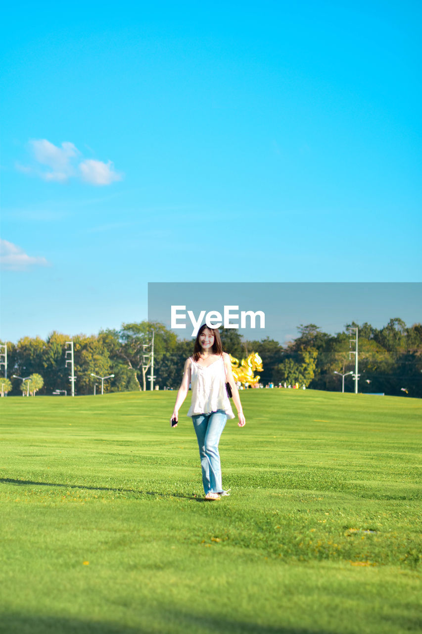 grass, full length, leisure activity, sports, plant, sky, adult, one person, casual clothing, green, activity, nature, golf, copy space, golf course, day, lifestyles, happiness, meadow, tree, sunlight, weekend activities, young adult, front view, women, emotion, standing, enjoyment, motion, outdoors, smiling, blue, field, lawn, relaxation, recreation, cheerful, sunny, female, men, summer, person