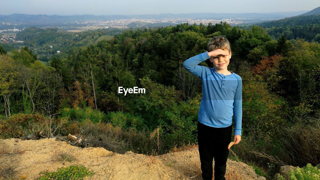 Portrait of boy standing on cliff against forest