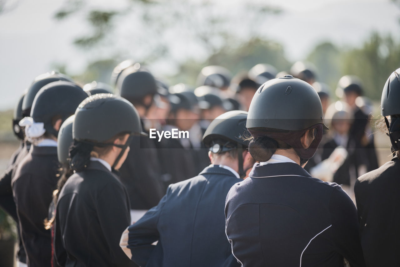 Group of anonymous jockeys in helmets standing in paddock on sunny day in equine club