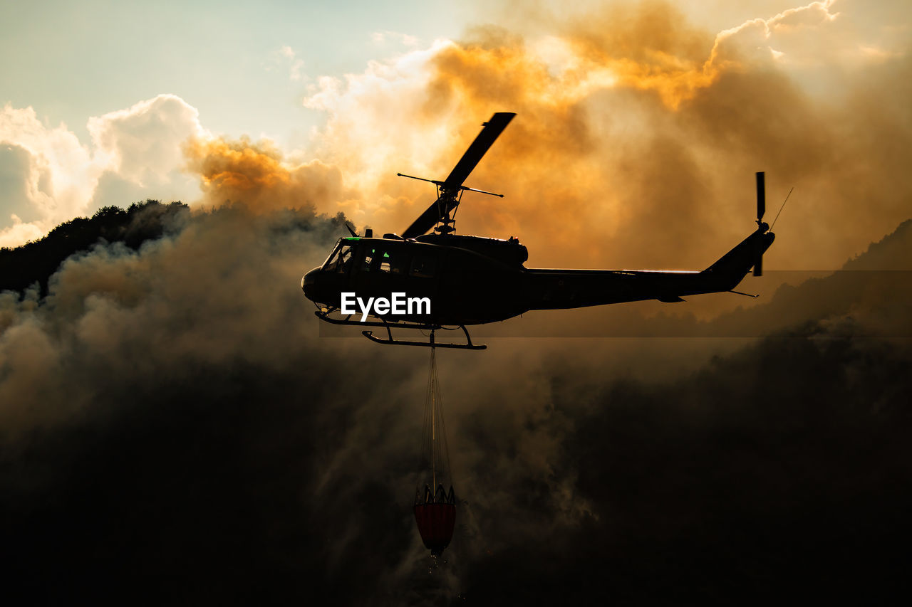 Low angle view of silhouette helicopter against smoke during sunset