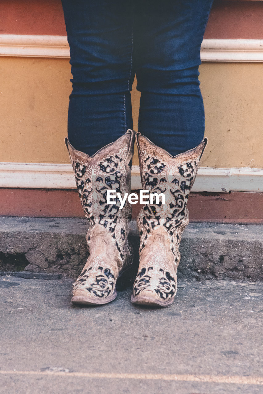 Low section of woman wearing cowboy boots standing against wall