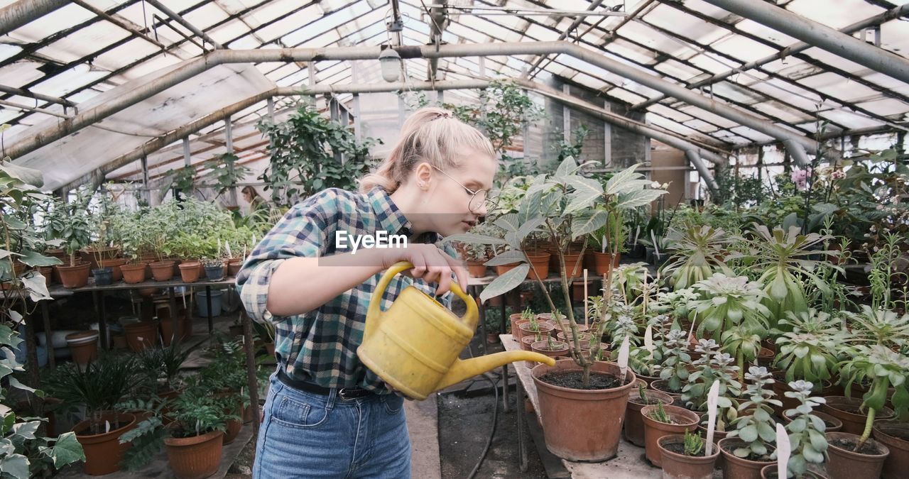 Caucusian woman holding a water can in greenhouse