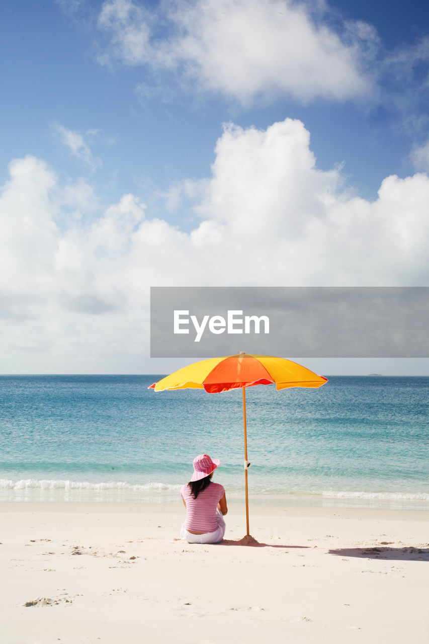 Woman relaxing on sand at beach against sky