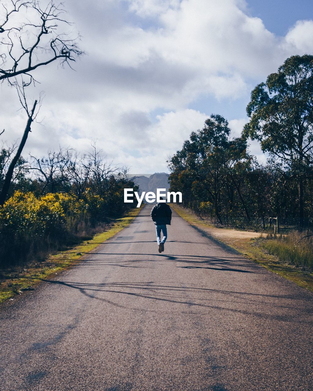 Rear view of man walking on road against sky