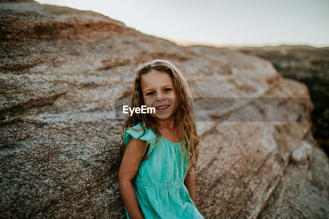 Young girl leaning against large rock