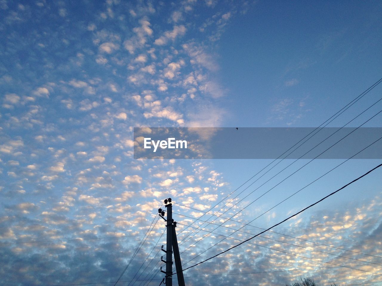 Low angle view of power lines against cloudy sky