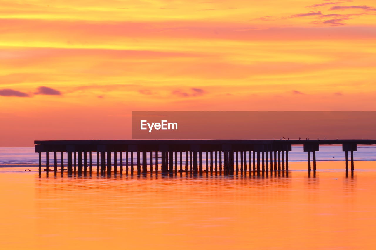 Silhouette pier on sea against orange sky