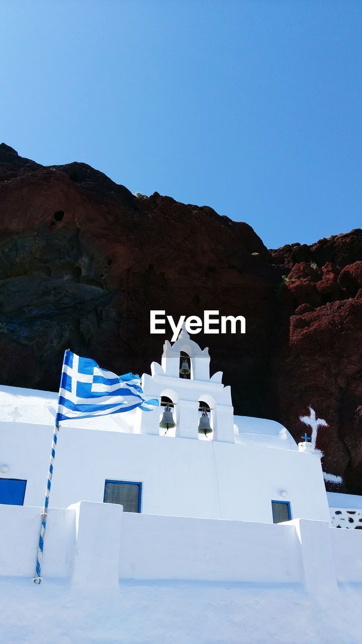 Low angle view of greek flag by bell tower against clear sky at santorini