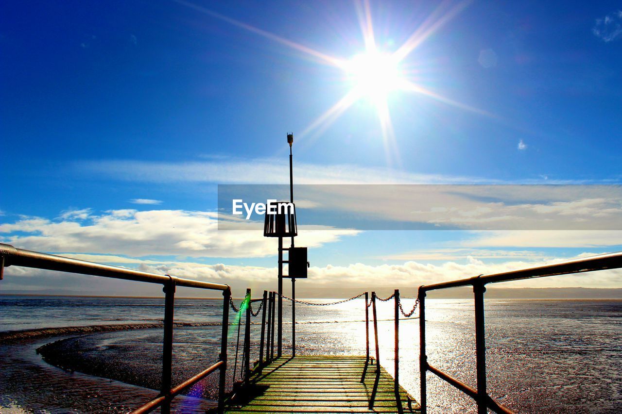 Pier over beach against bright sky