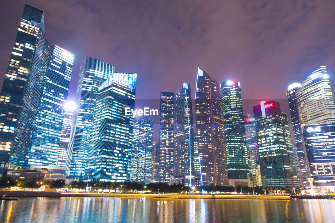 Illuminated buildings by river against sky at night