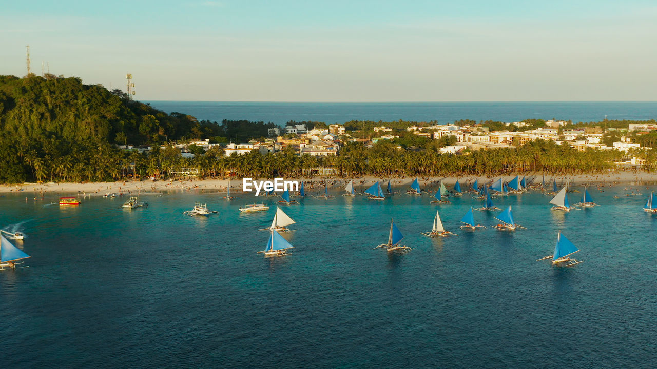 Topical white beach from above at sunset with tourists and hotels and sailing boats on boracay