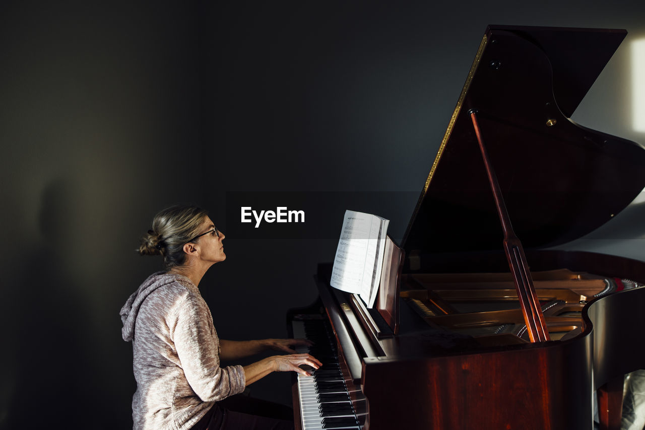 Side view of mature woman playing piano at home