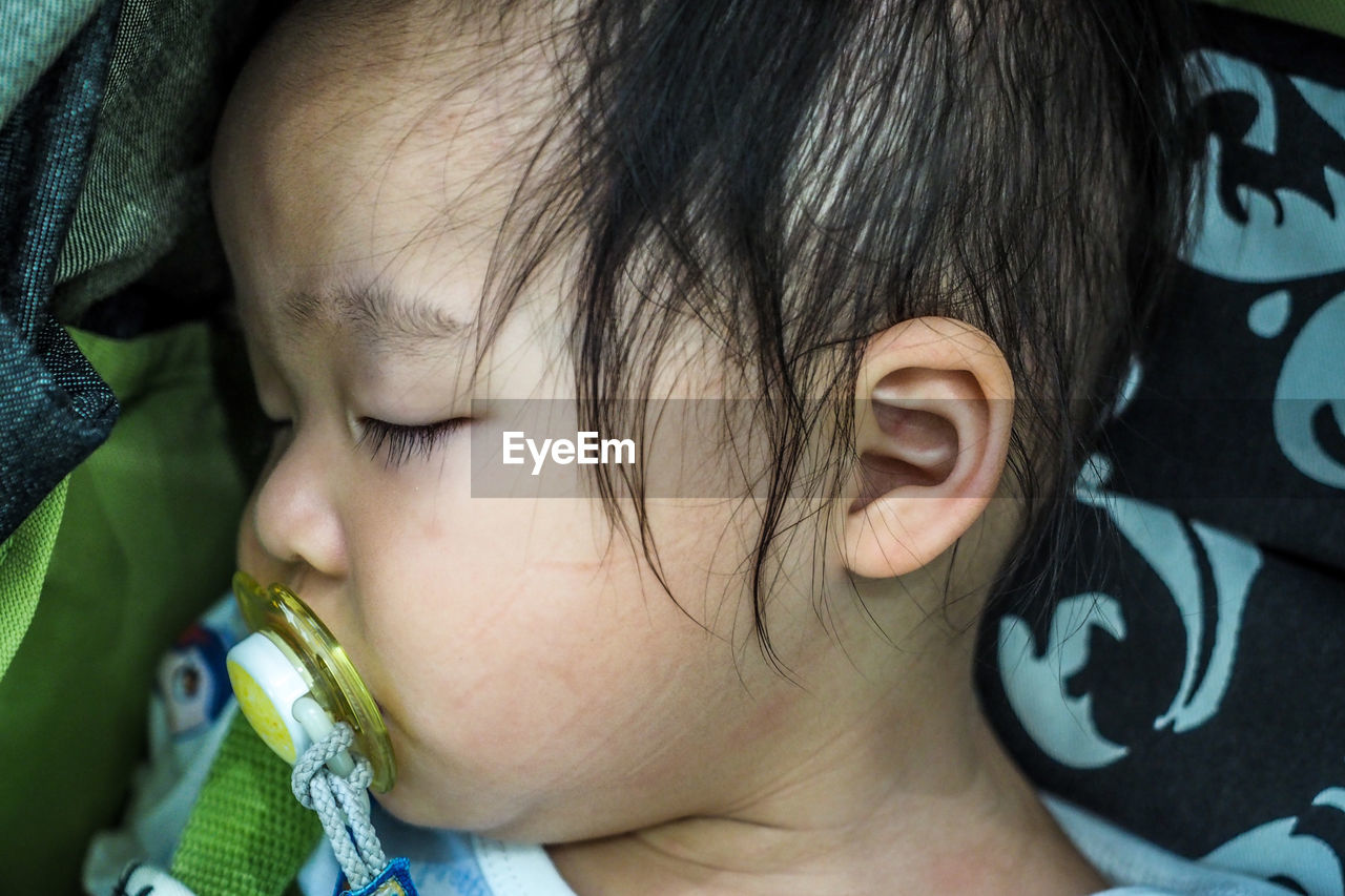 Close-up of cute girl with pacifier sleeping on bed