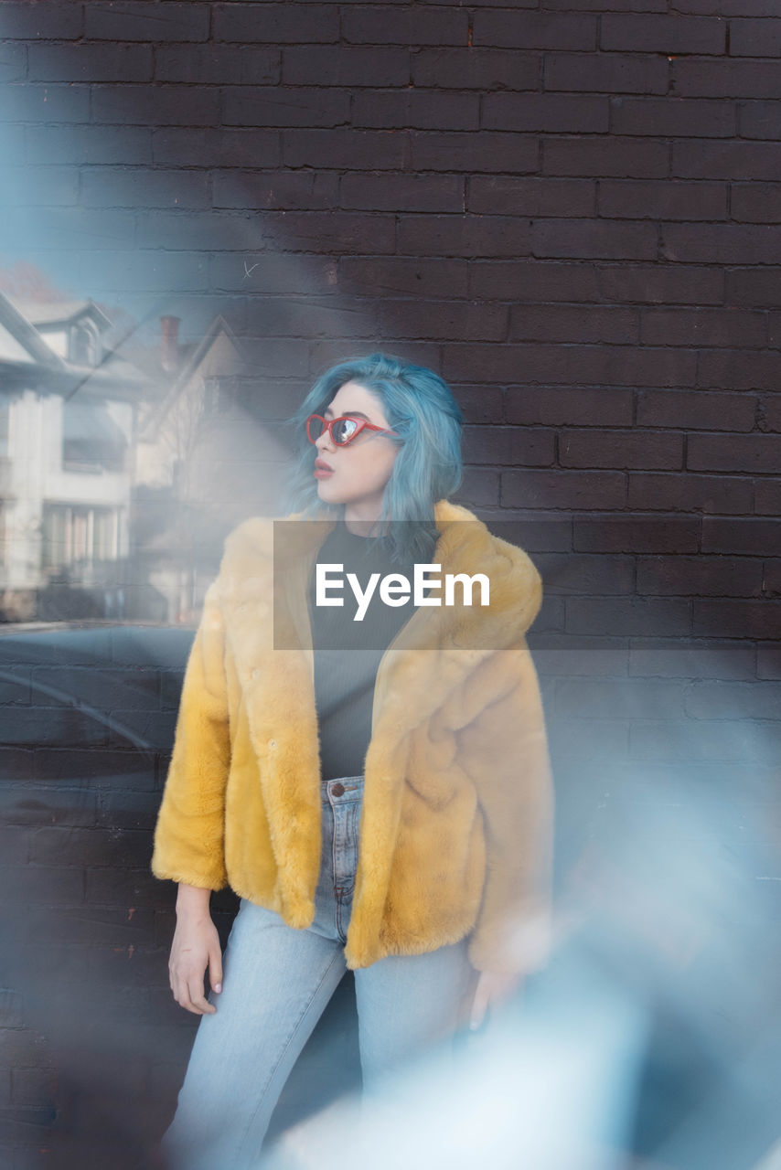 Sunlight falling on woman wearing yellow jacket while standing against wall