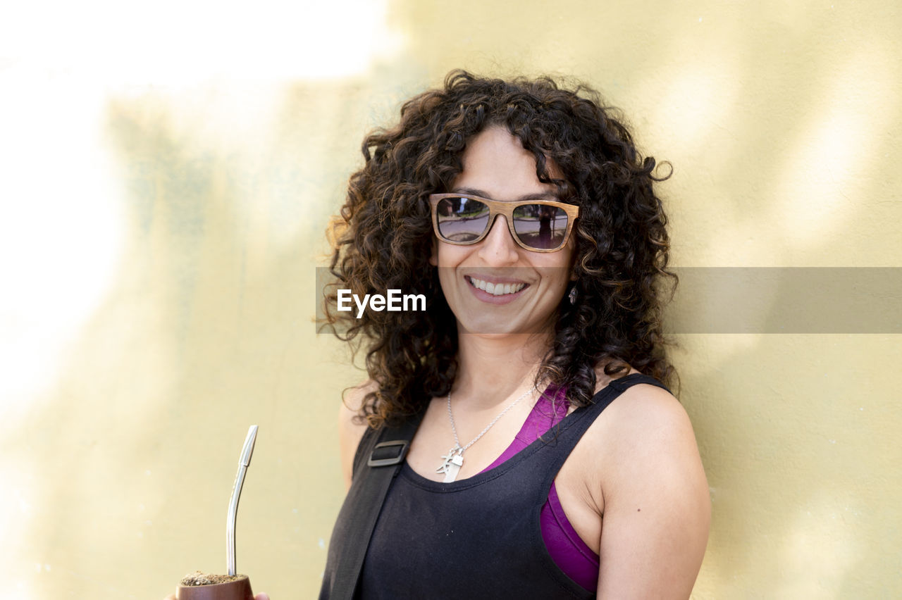 Mixed race woman smiling while drinking mate outdoors.