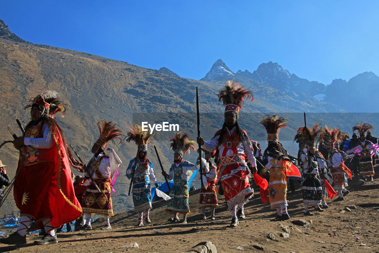 People in traditional clothing dancing on sand against mountains and sky
