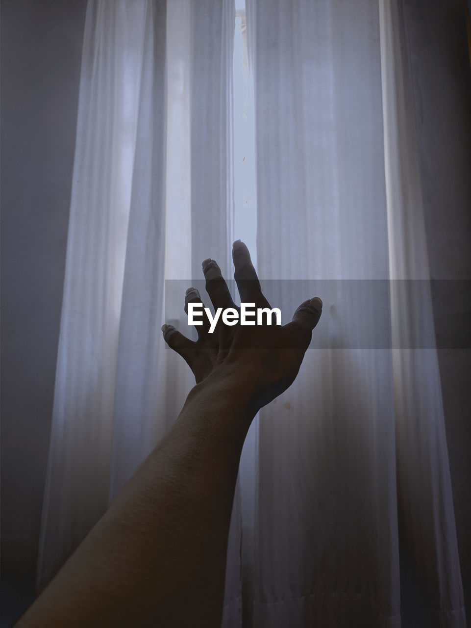 Close-up of hand against curtains at home