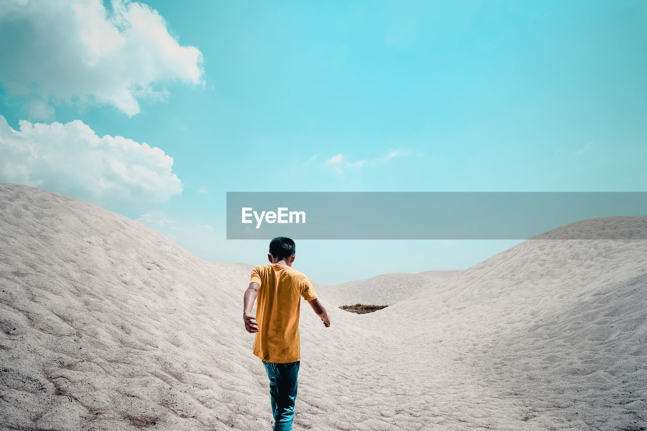 Rear view of boy walking at desert against blue sky