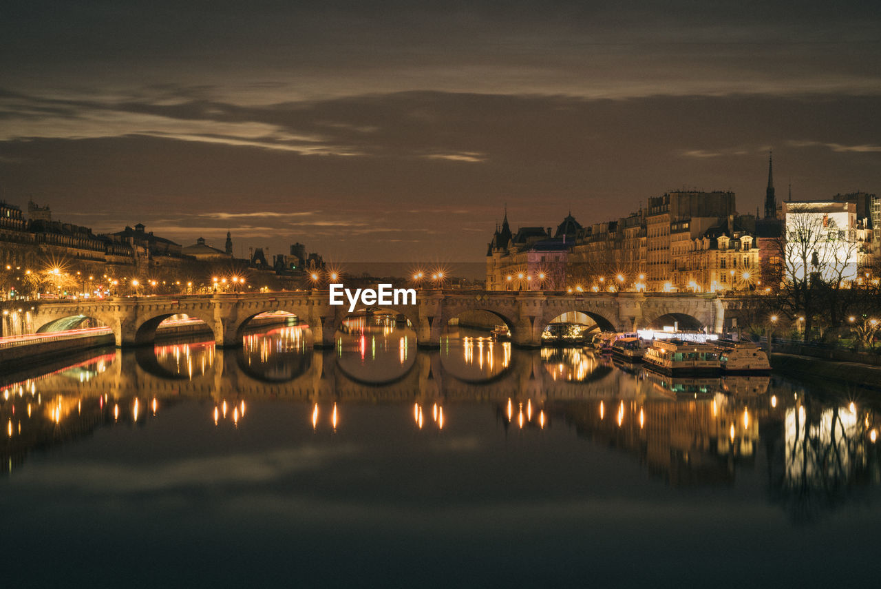 Illuminated pont neuf over seine river amidst buildings against sky at night