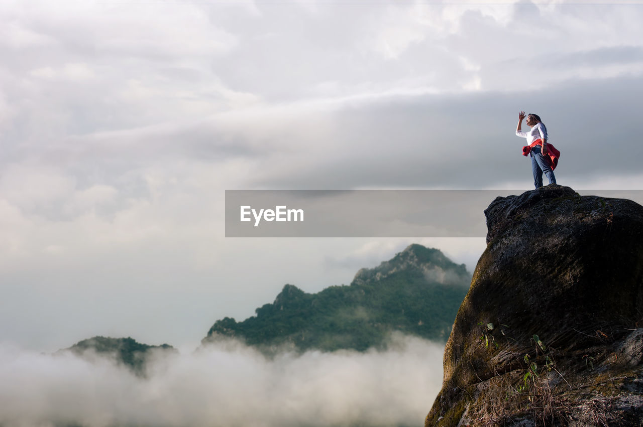 Low angle view of woman standing on cliff against sky