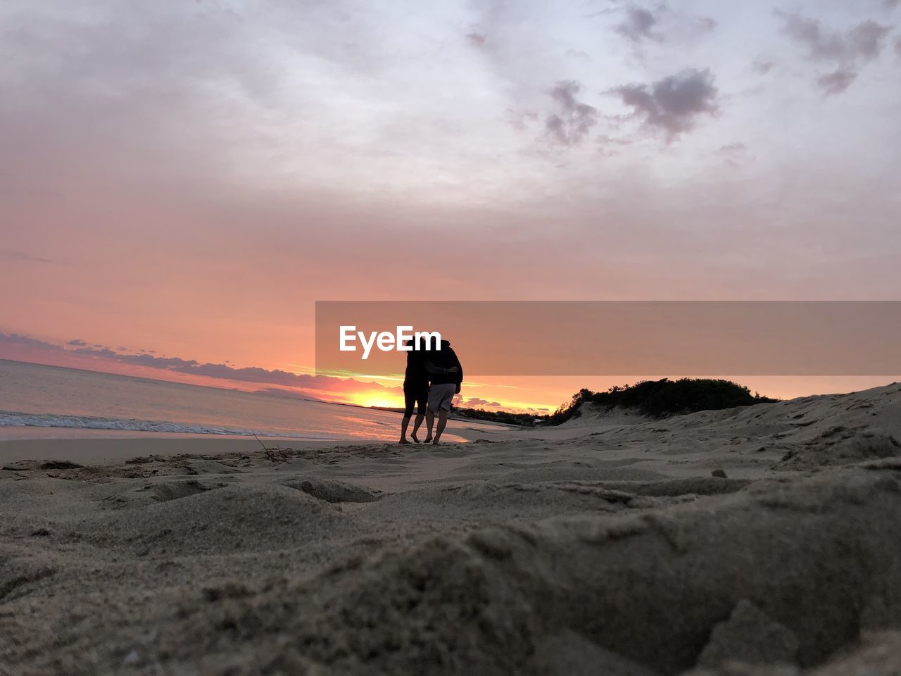 REAR VIEW OF MAN ON BEACH DURING SUNSET