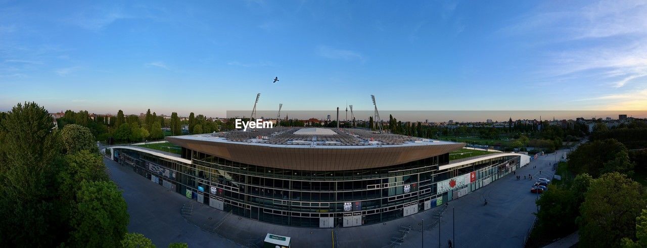architecture, sky, built structure, sport venue, building exterior, panoramic, stadium, city, nature, reflection, landmark, travel destinations, blue, travel, cloud, sports, sunset, building, outdoors, plant, high angle view, cityscape, water, arena, arts culture and entertainment, no people, business finance and industry, environment, tourism, landscape, tree, history