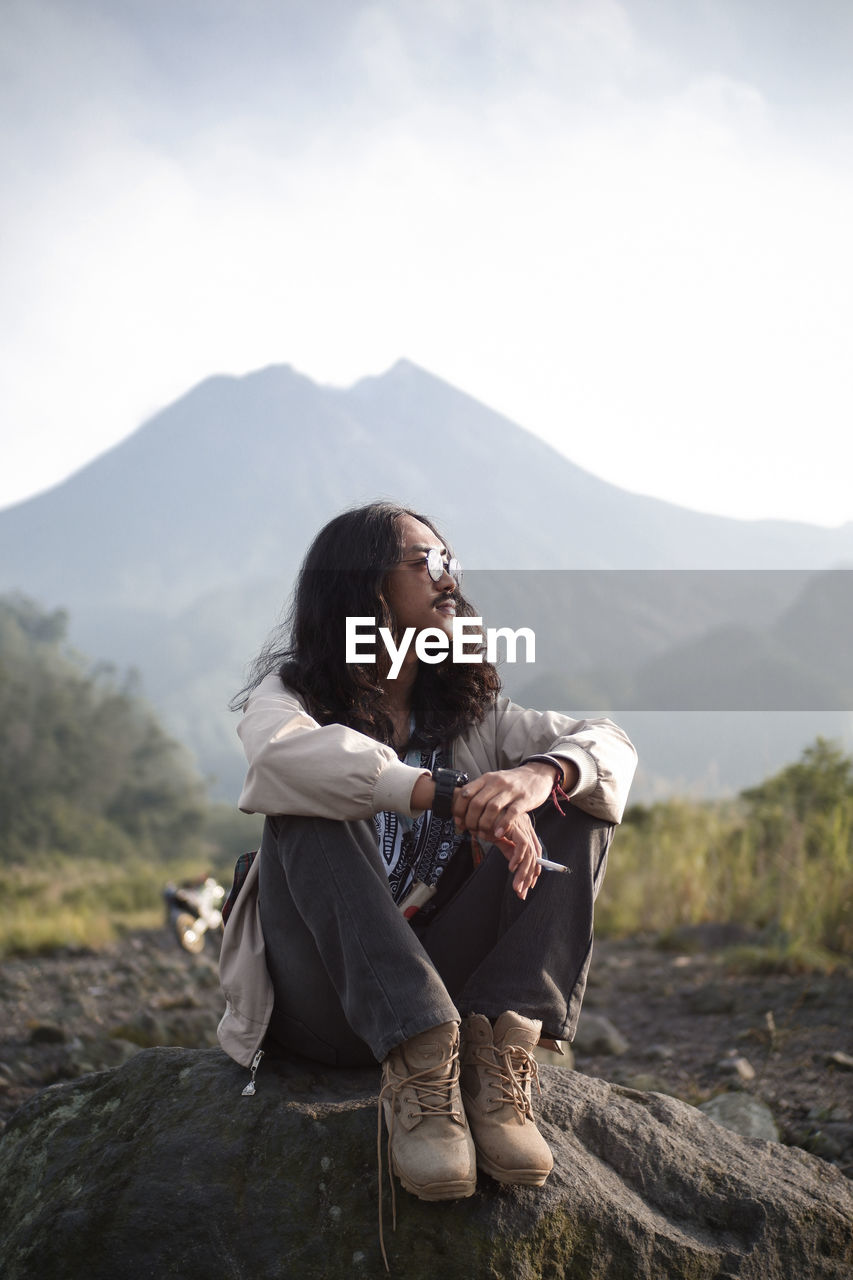 Young woman sitting on mountain against sky