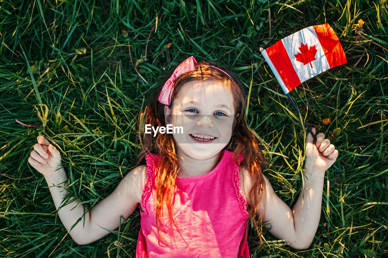 Happy girl with canadian flag lying on field