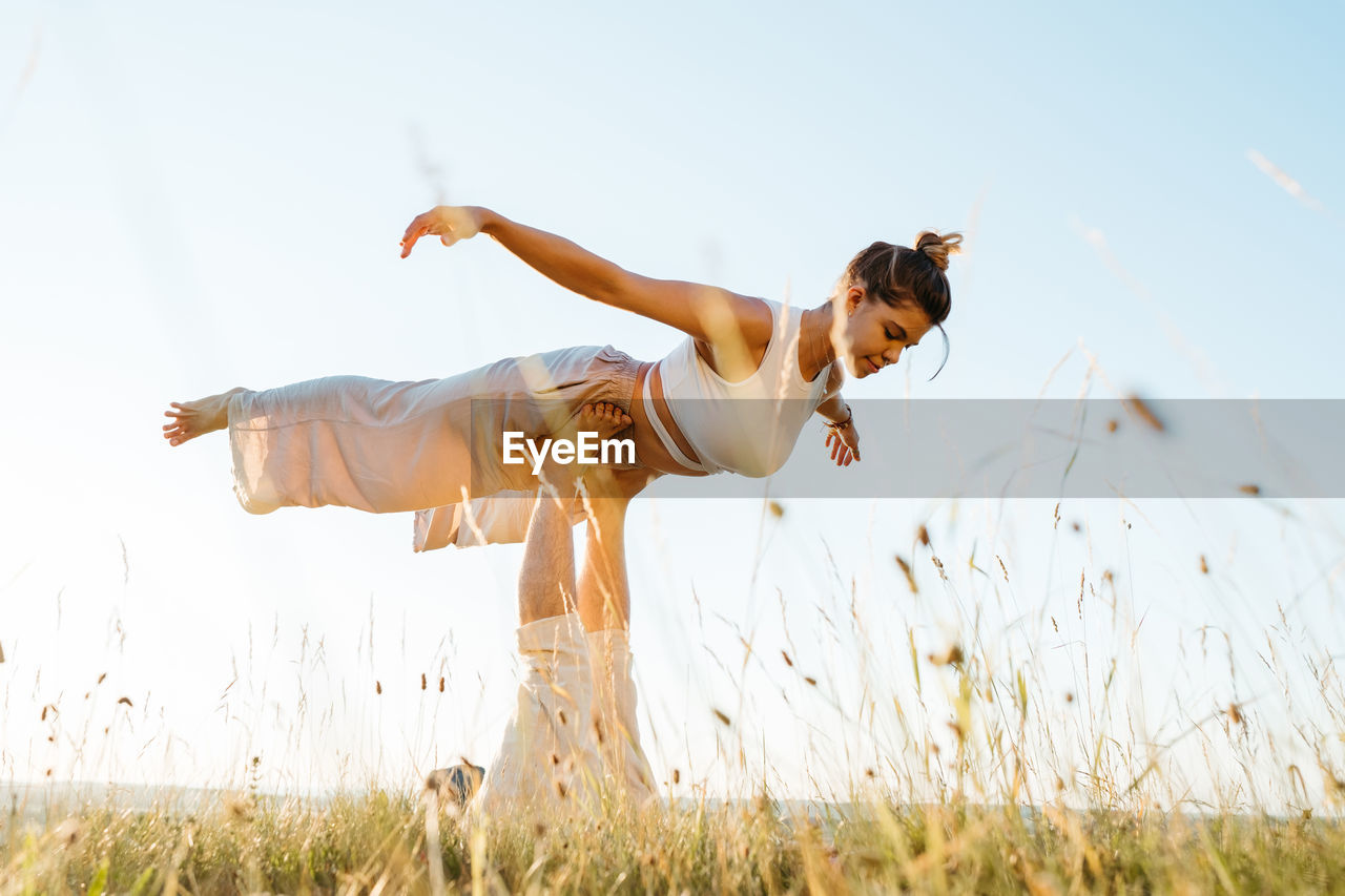 Couple making beautiful pose, man and woman practicing yoga outdoors at sunset