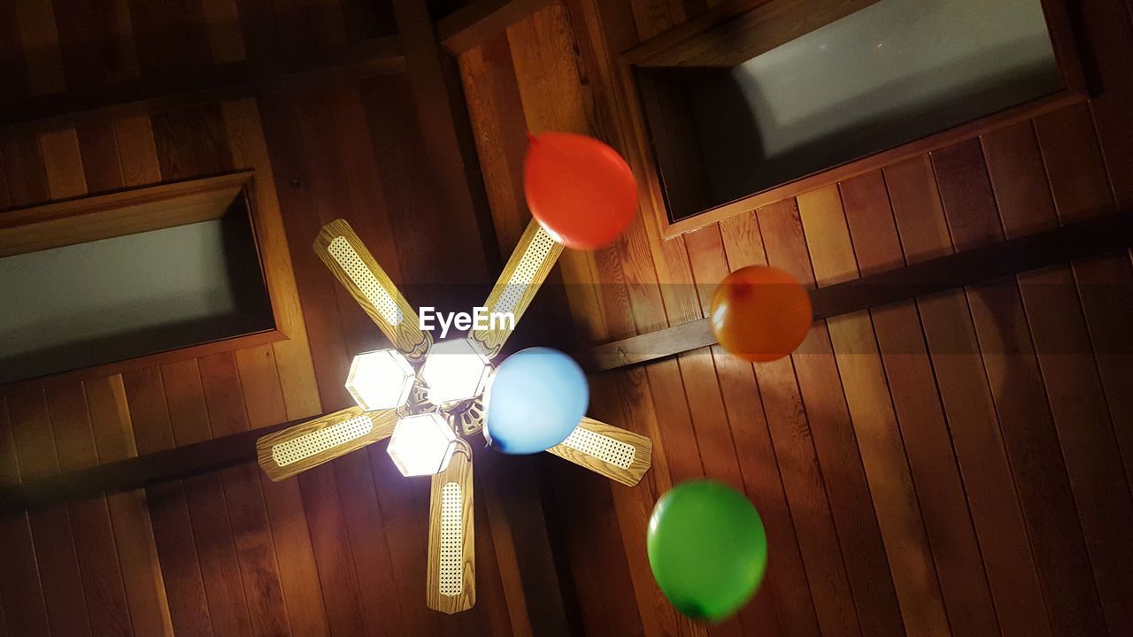 Directly below view of helium balloons with illuminated pendant light on ceiling fan
