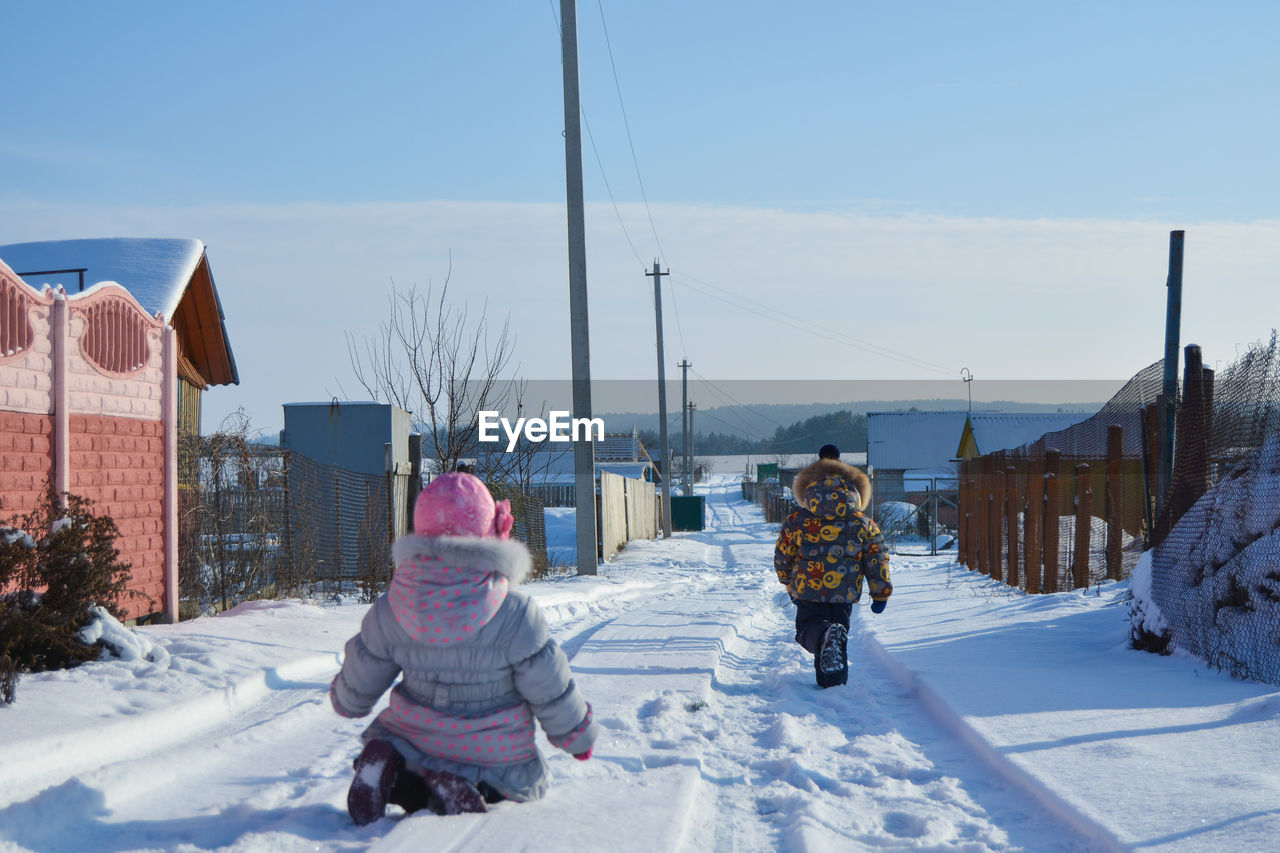 Rear view of kids on snow covered road against sky