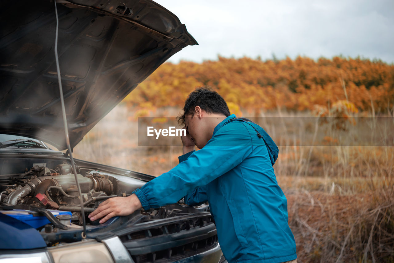 Side view of man standing by car on road