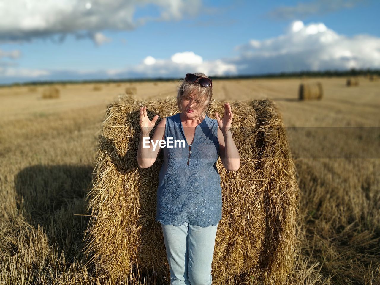 Midsection of woman with hay bales on field against sky