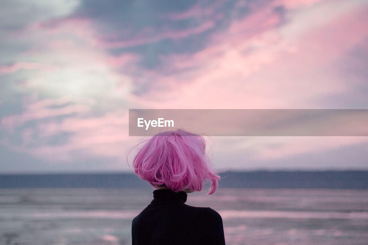 Woman with pink hair standing at beach against sky during sunset