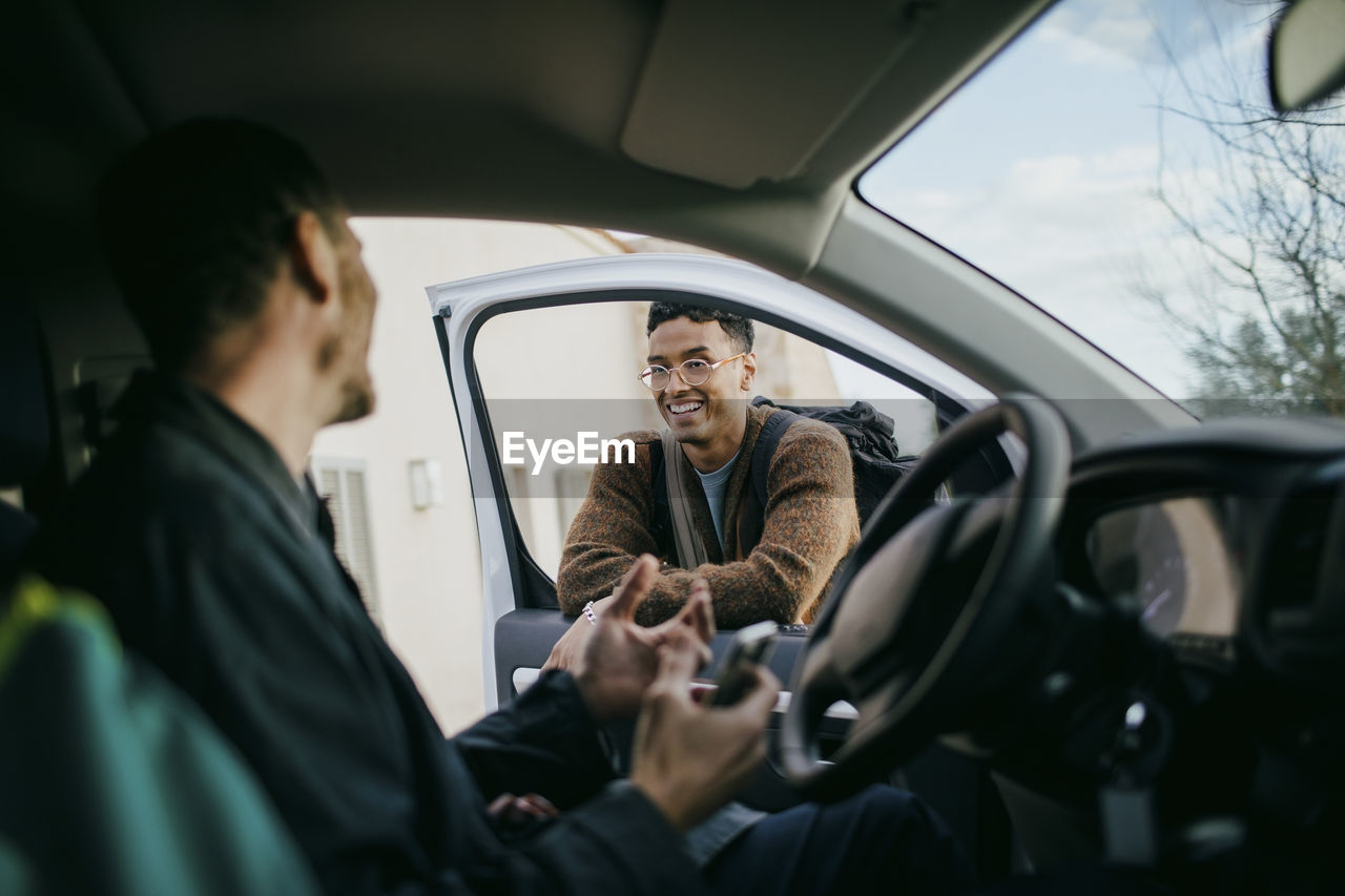 Smiling man looking at friend sitting inside of van