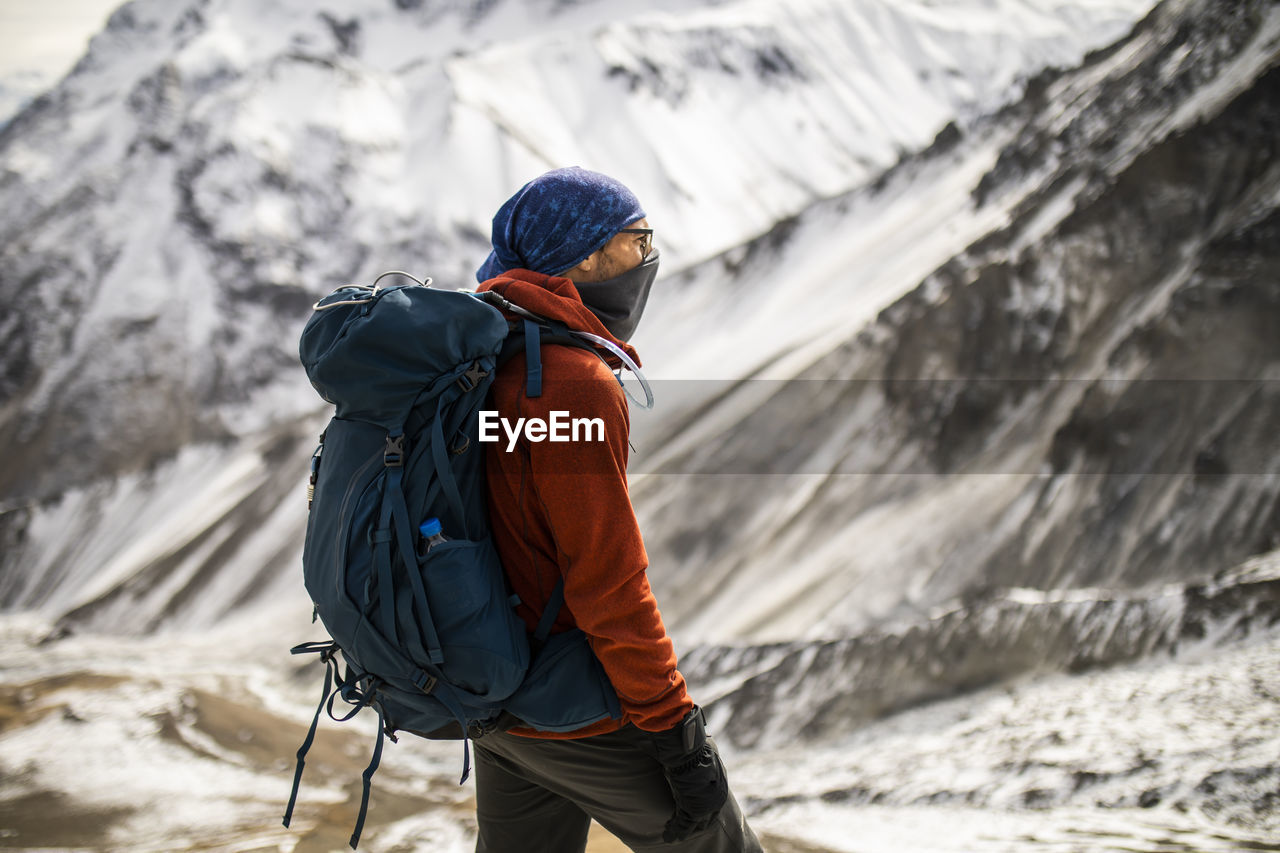 Side view of male hiker in warm outerwear standing on hill on background of snowy himalayas mountains in winter in nepal