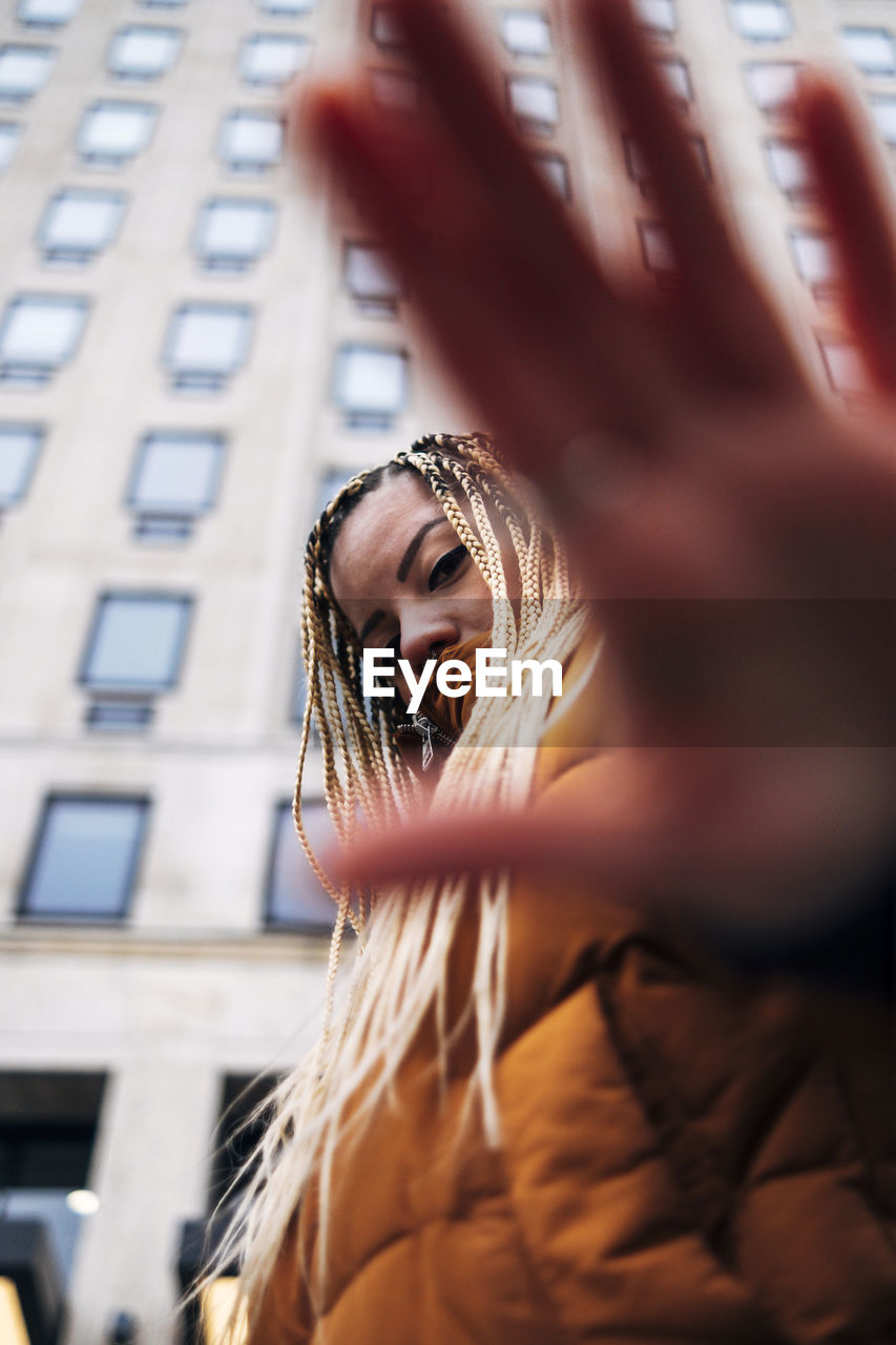 Woman stretching hand while standing against building