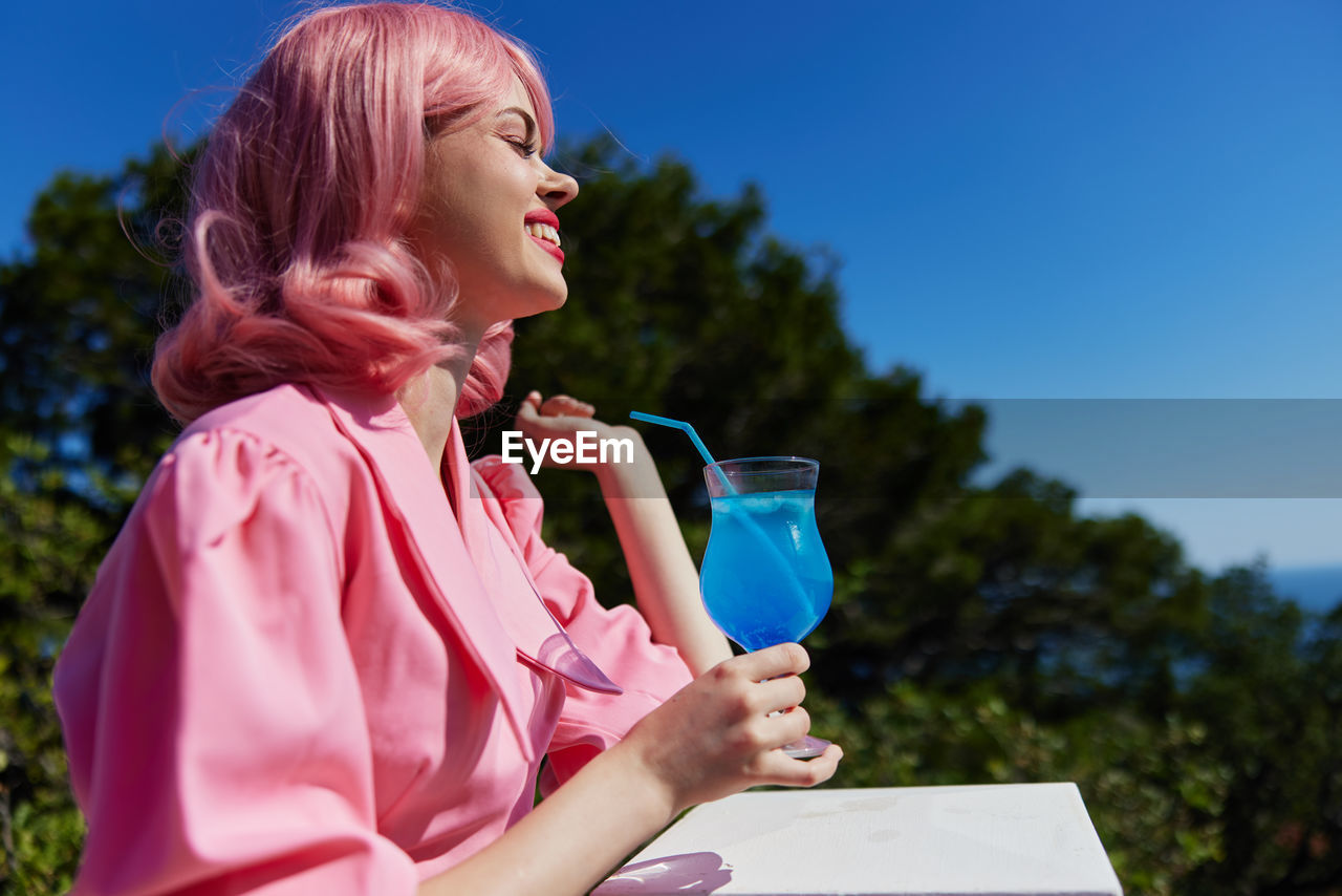 Smiling woman holding cocktail against trees