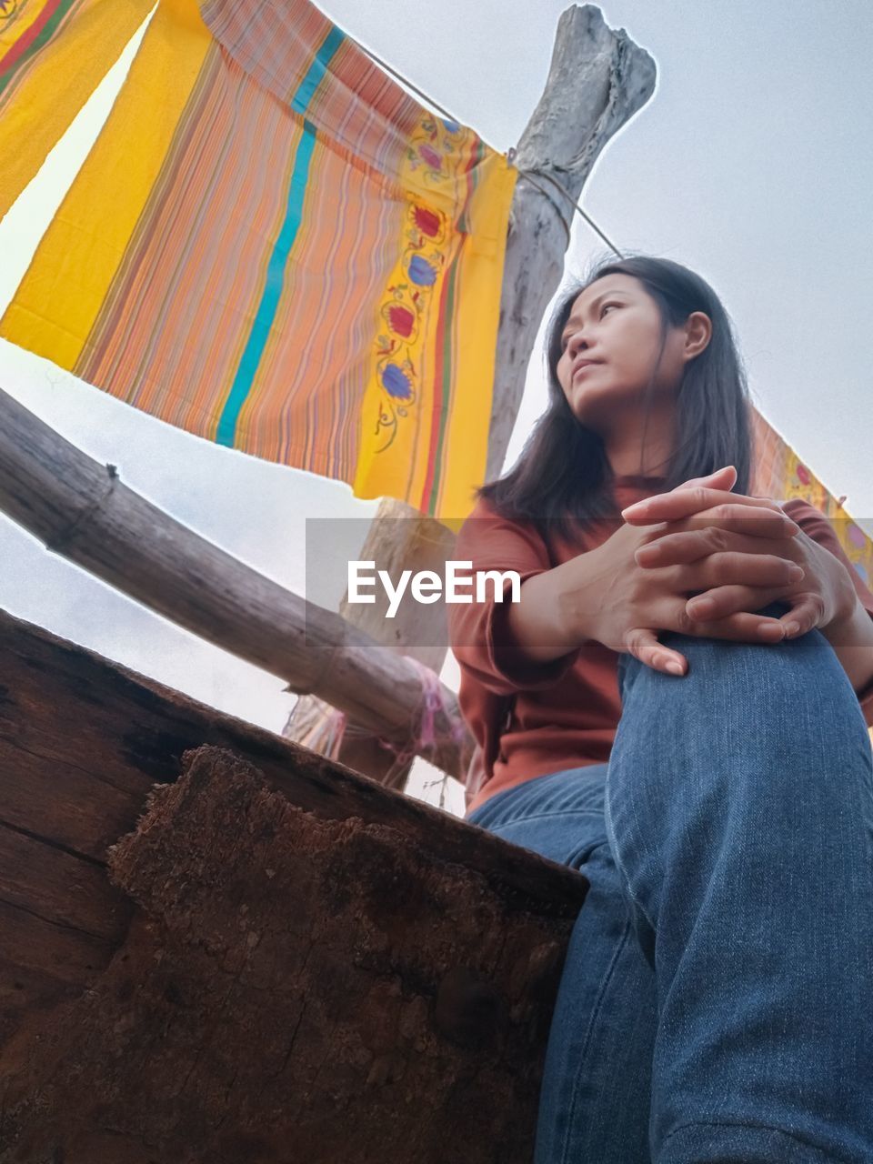 YOUNG WOMAN LOOKING WHILE SITTING ON WALL