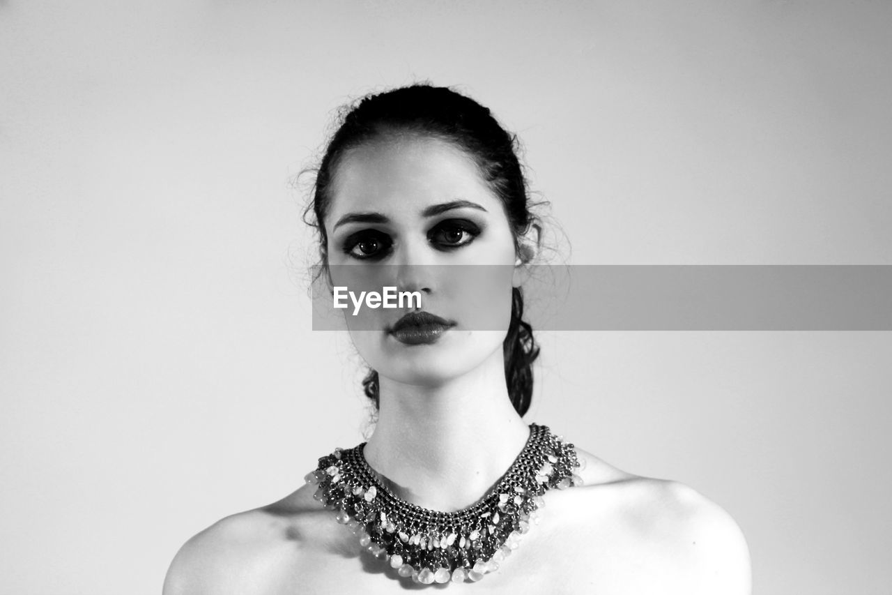 Portrait of shirtless woman wearing make-up and necklace against white background