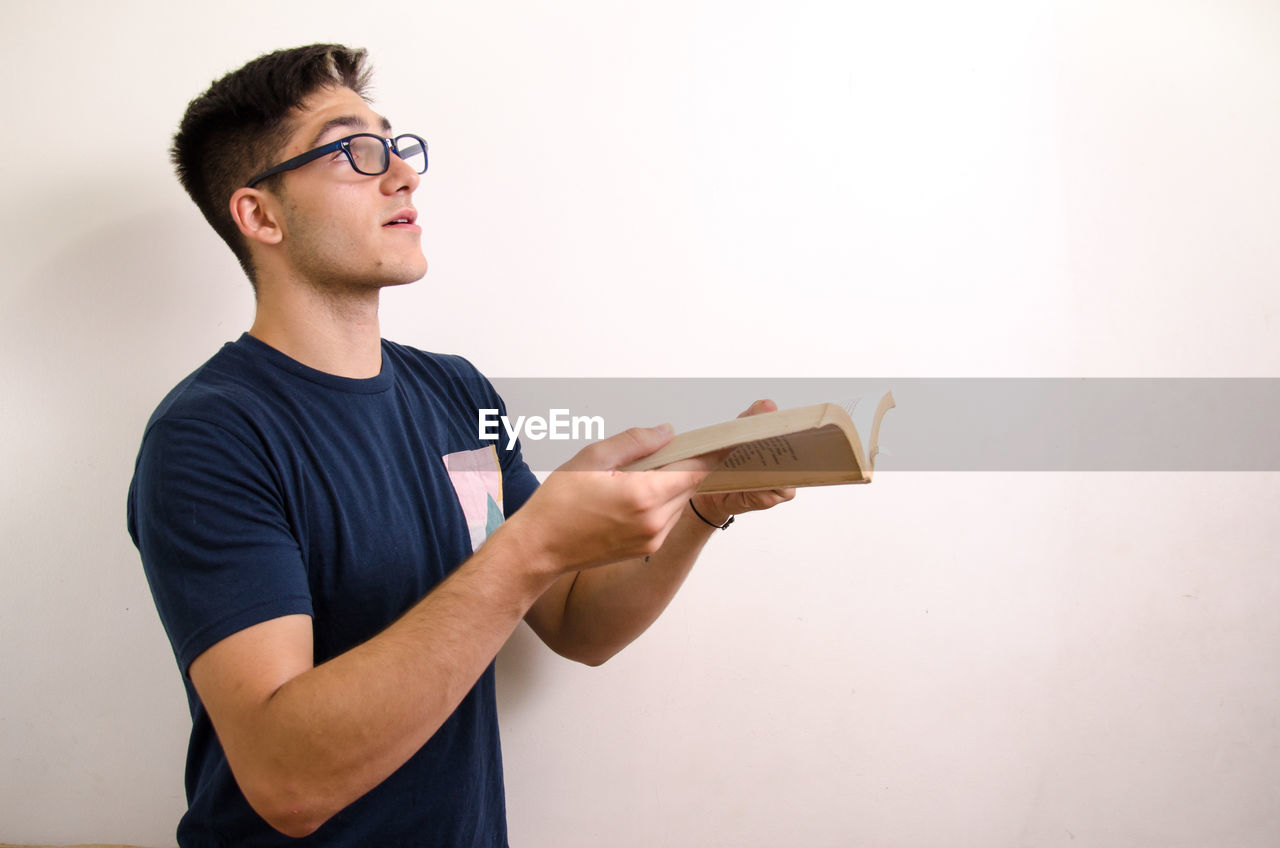 YOUNG MAN LOOKING AWAY WHILE STANDING BY WALL