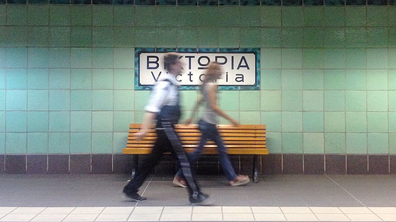 Man and woman walking by tiled wall at railroad station