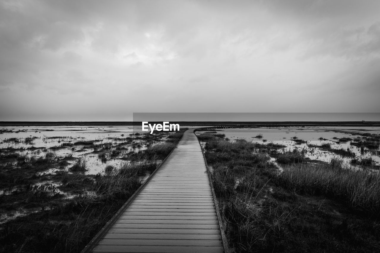 WOODEN BOARDWALK ON BEACH AGAINST SKY