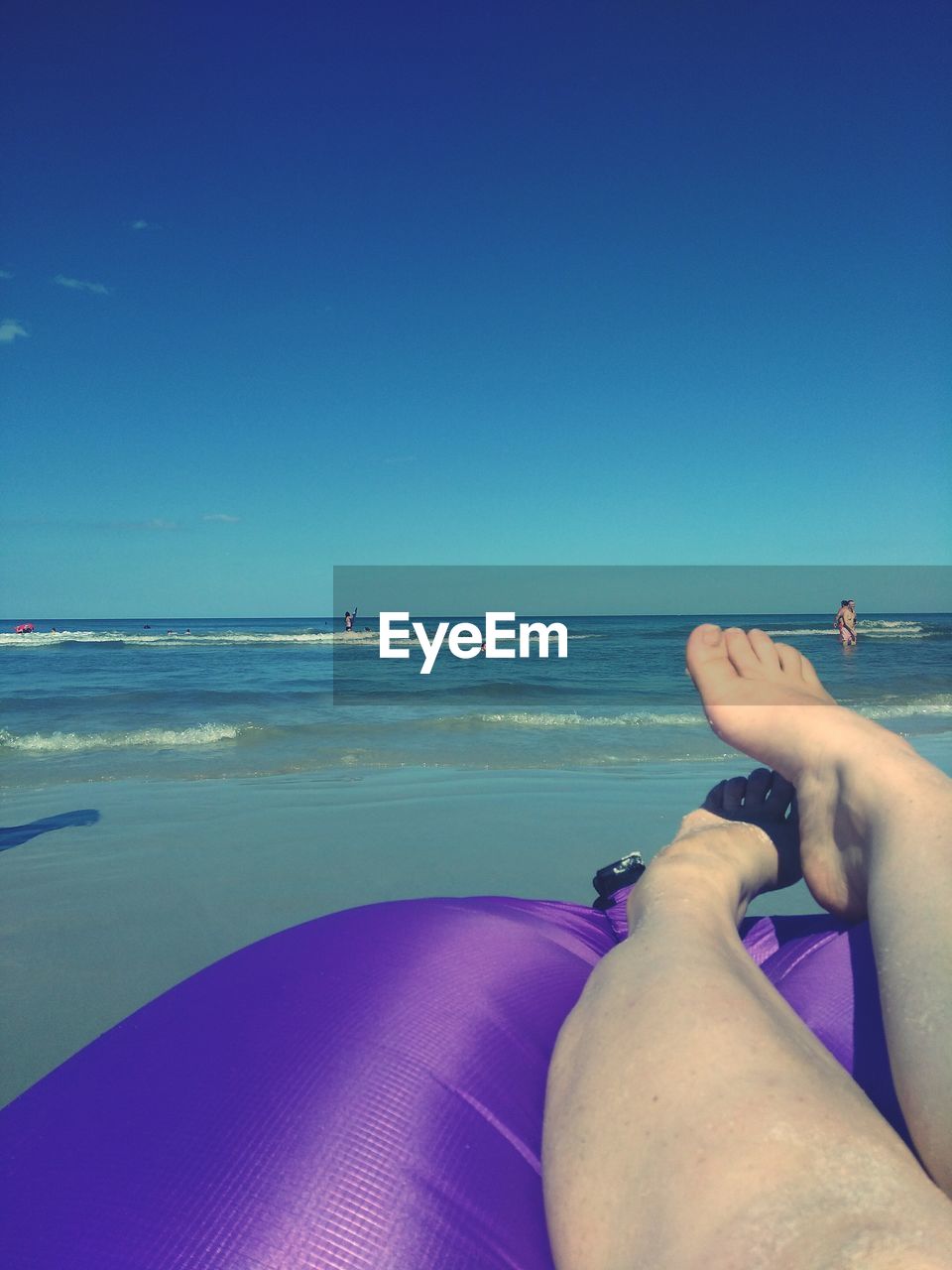 Low section of woman on beach against clear blue sky