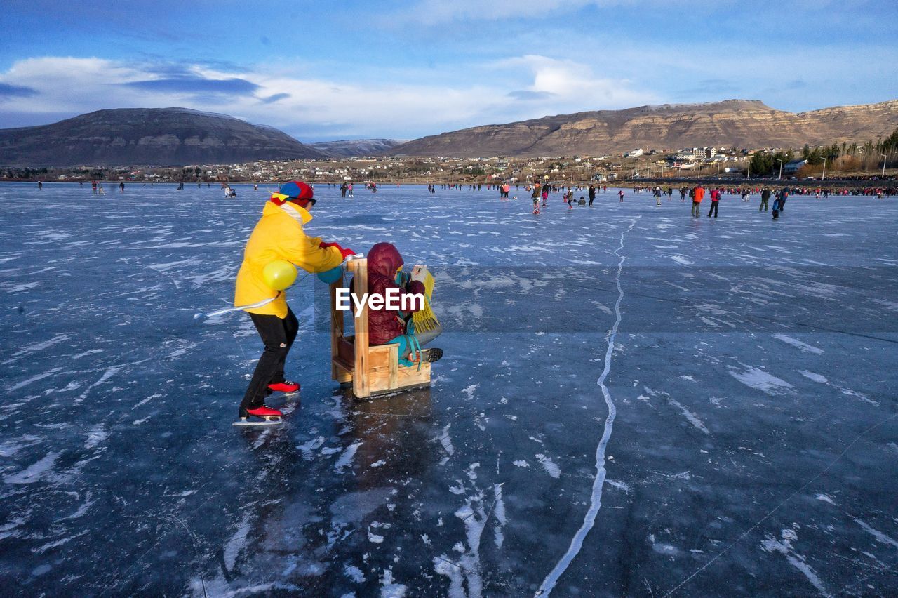 People on frozen lake against sky