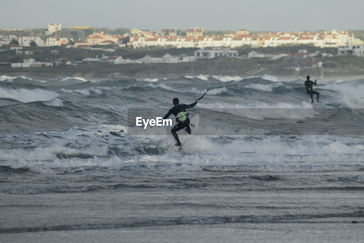 Men surfing in sea against sky