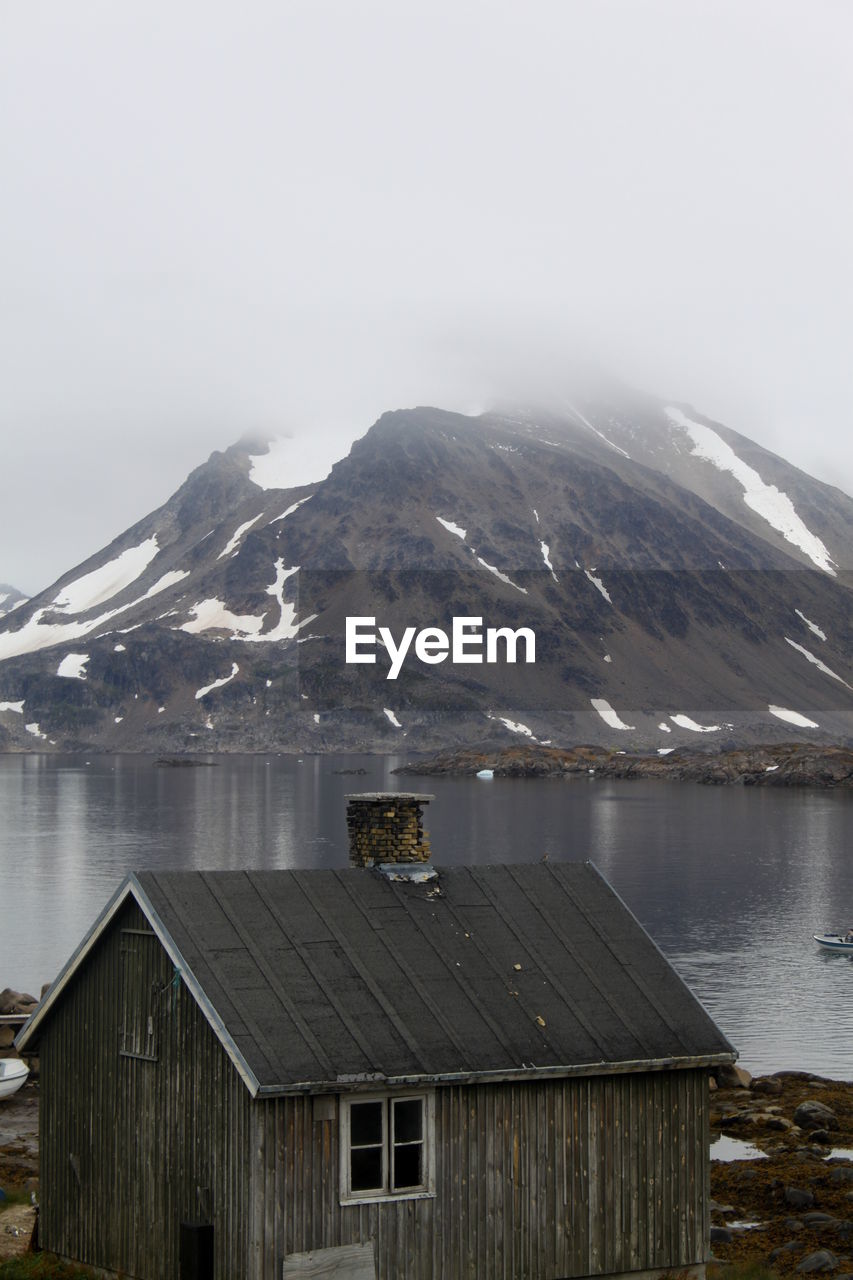 Wooden house by lake against mountain in winter