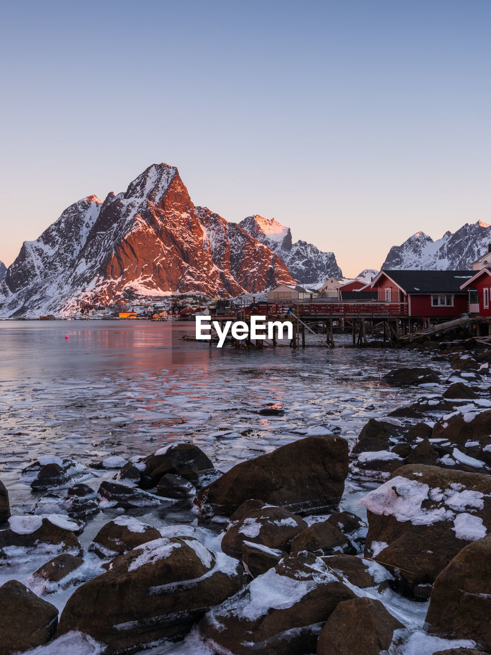 Scenic view of lake by snowcapped mountains against sky during sunset