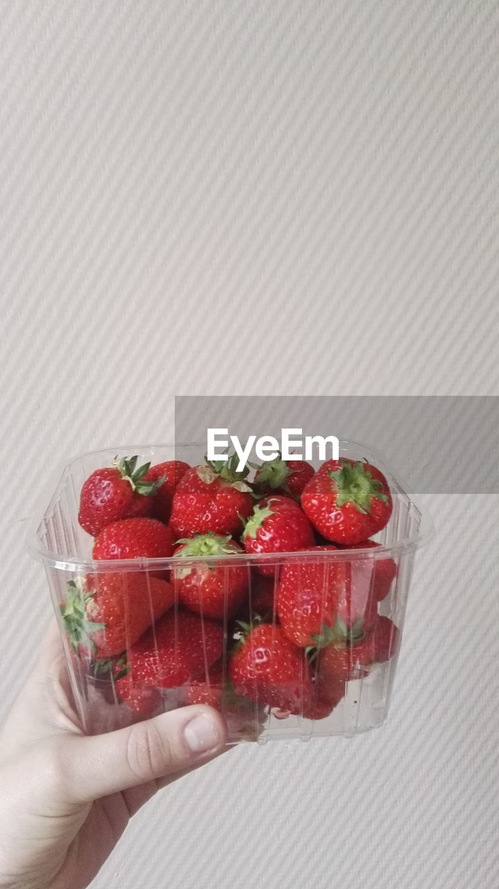 Close-up of hand holding strawberry over white background