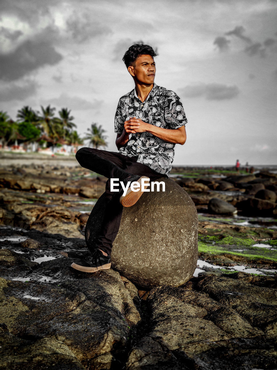 Full length of man sitting on rock looking away against sky